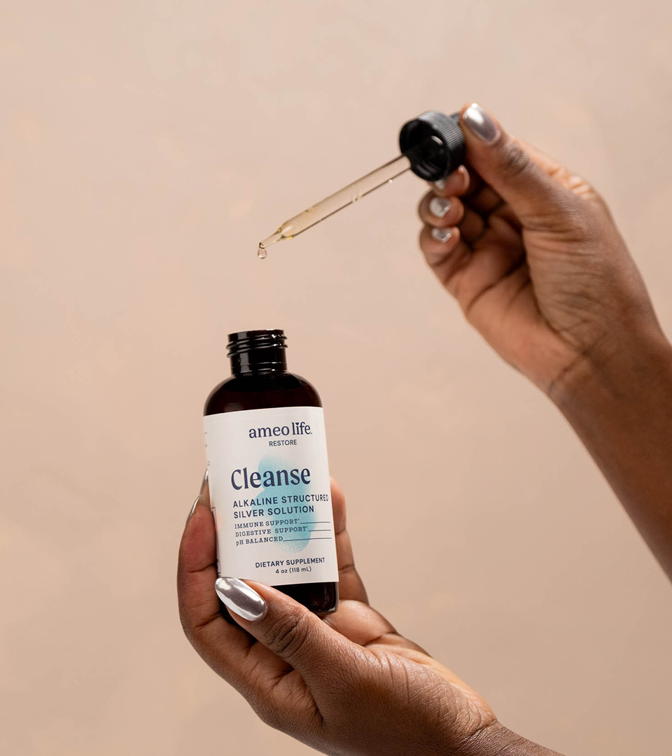 Ameo Life Cleanse supplement in hand Hand holding an Ameo Life Cleanse supplement bottle with dropper.