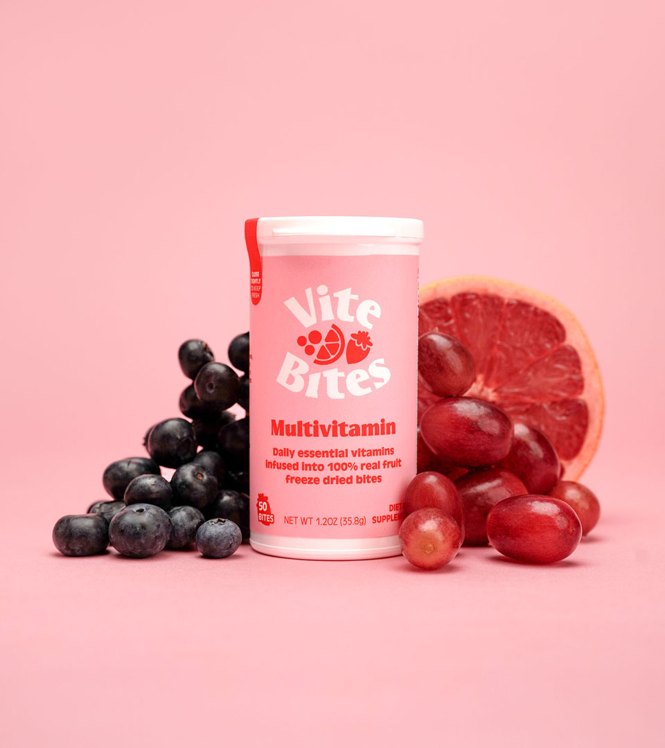 ViteBites Multivitamin Packaging ViteBites Multivitamin container displayed with blueberries and grapefruit on a pink background